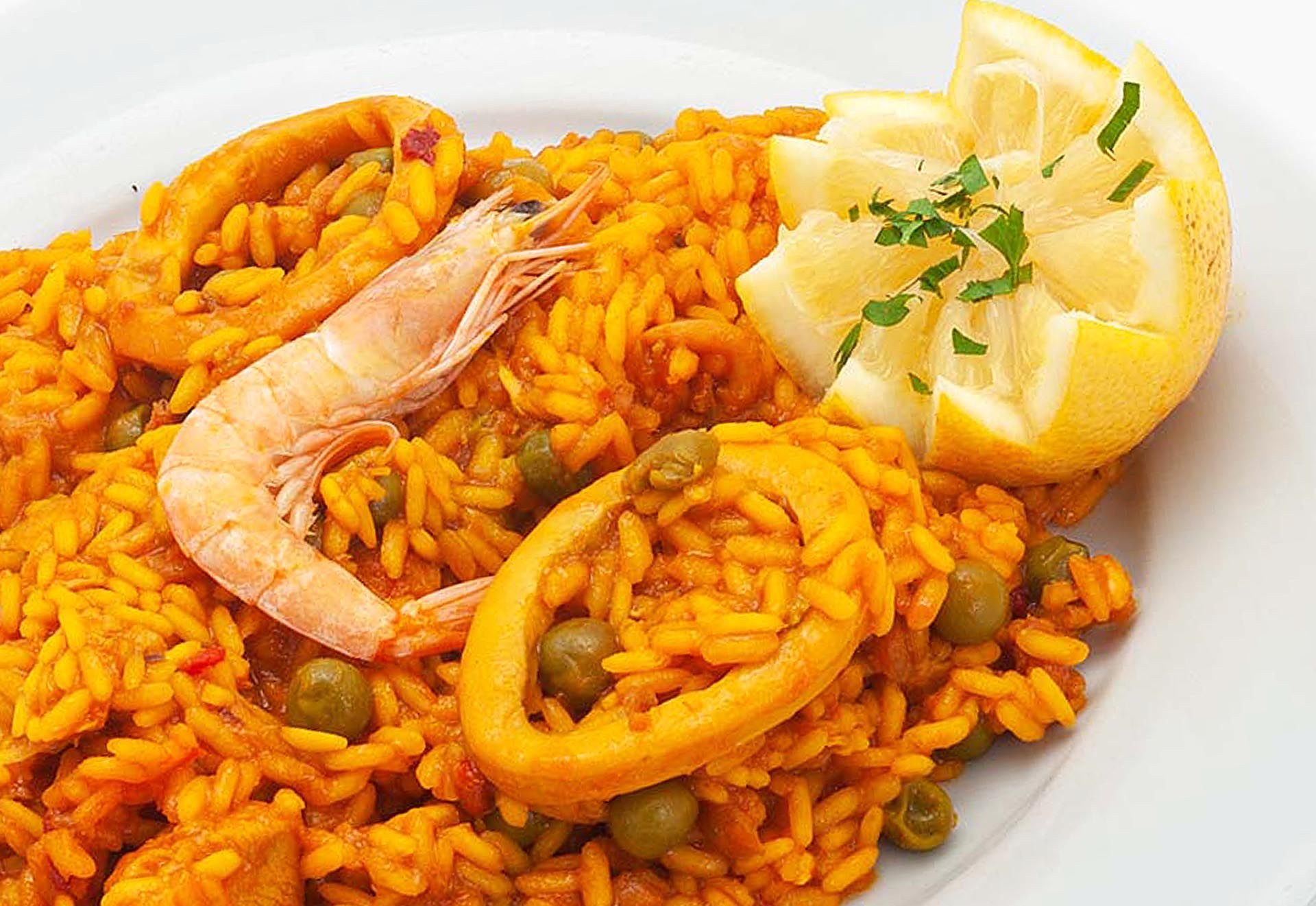 Plato de arroz con gambas, calamares guisantes y limón